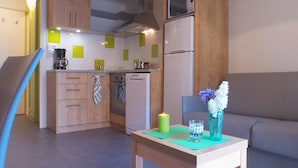 Een compacte keuken met houten kastjes, een magnetron en een koelkast. Er staat een klein tafeltje met een kaars en een bloemenvaas.