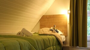 Een knus vertrek met een schuine kap, een bed met groene beddengoed, een comfortabele bank en een kopje op een schoteltje op een tafel.