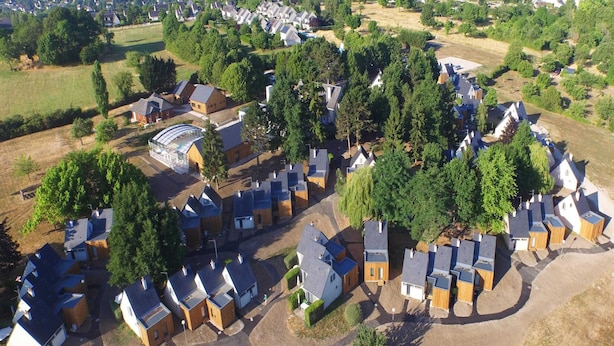 Luchtbeeld van een woongebied, met huizen in een halve cirkel, omgeven door bomen en open velden.