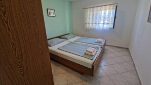 A room with two single beds, a window with sheer curtains, and a wooden door.