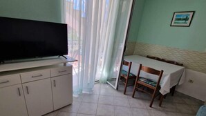 A room with a TV on a cabinet, a dining table with chairs, and a window with curtains.