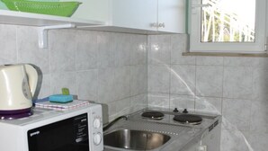 A compact kitchen with a microwave, a kettle, a sink, and a window.