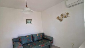 A room with a sofa, a pendant light, a wall-mounted air conditioner, and a decorative wall piece.