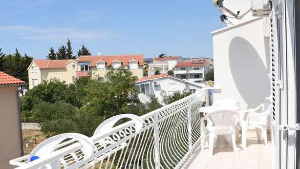 A balcony with white chairs and a white railing overlooking a residential area with houses and trees.