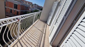 A balcony with a white railing, a door with white shutters, and a view of neighboring buildings.