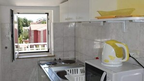 A compact kitchen with a gas stove, a microwave, and a yellow kettle. A window with a view of a red building is visible.