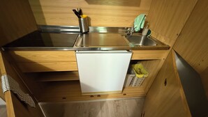 Cocina compacta con un lavamanos de acero inoxidable, una pequeña encimera y un electrodoméstico blanco.