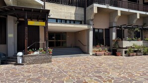 Entrada de hotel con un patio de baldosas de piedra, una escalera que conduce a la entrada y plantas en macetas alrededor del área.