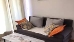 A living room with a sofa, two pillows, and a table with a floral tablecloth. - Apartment Belu - Two Bedroom Apartment With Sea View (Brodarica)