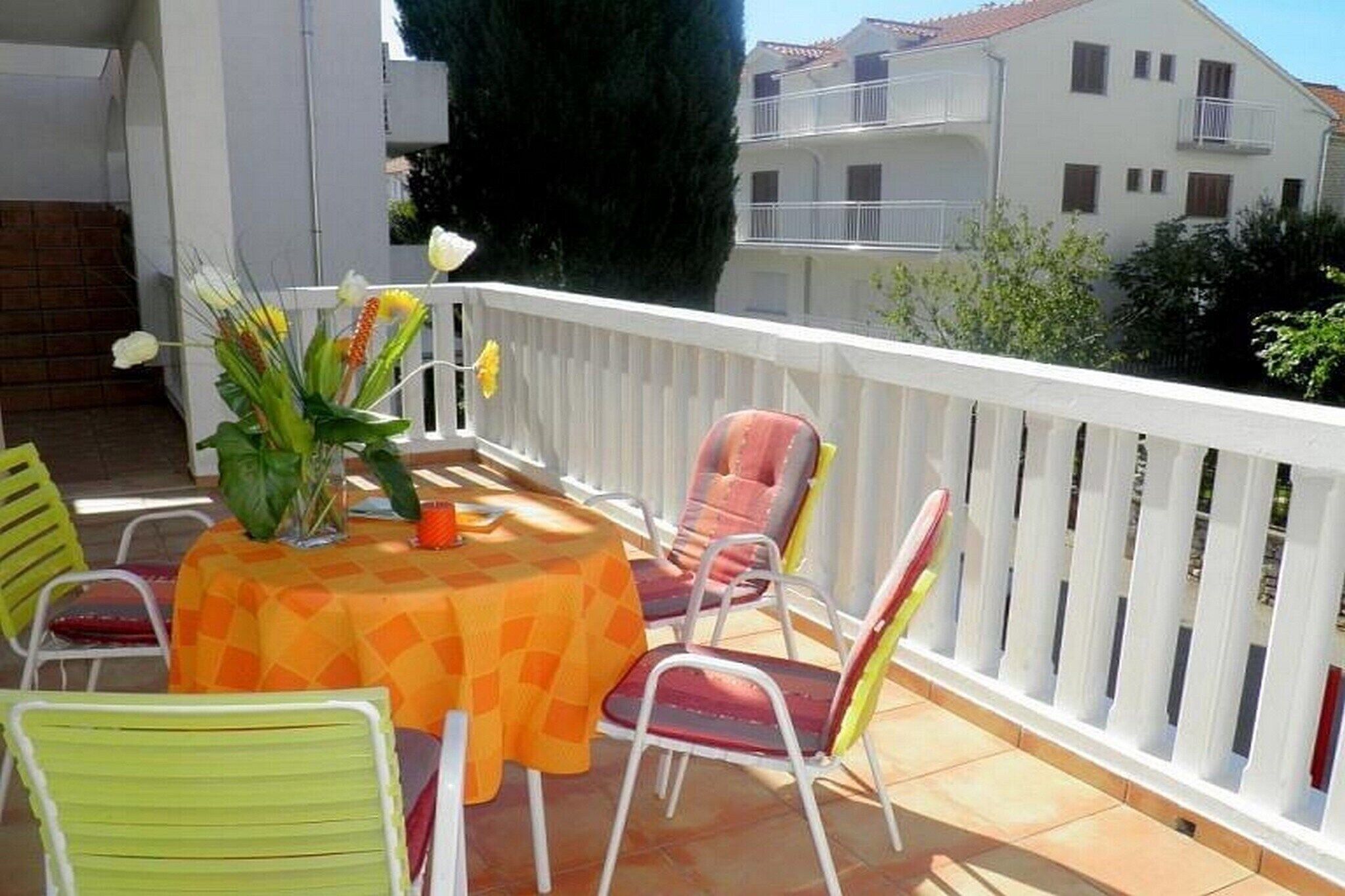 A balcony with a table and chairs, a white fence, and a building in the background.