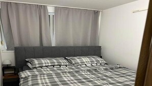 Un dormitorio con cama, cortinas grises y pared blanca.
