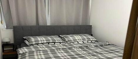 A bedroom with a bed, grey curtains, and a white wall.