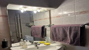 Un baño con un lavamanos blanco, un espejo y dos toallas moradas colgadas de ganchos.