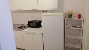 A compact kitchen with white cabinets, a sink, a black microwave, and a white refrigerator.