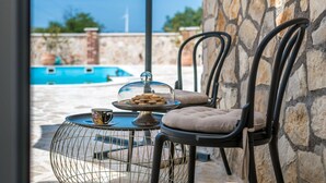 A poolside area with stone walls, a round table with a glass dome, and two cushioned chairs.