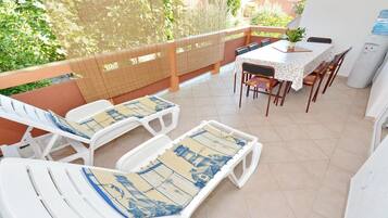 Ein Balkon mit weißen Liegestühlen, einem Tisch mit Stühlen und einem Wasserspender.
