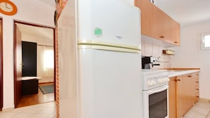 Een kleine keuken met een witte koelkast, een fornuis en houten kastjes.