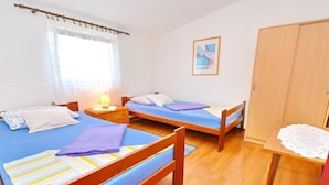Een kamer met twee eenpersoonsbedden, houten hoofdborden, een klein tafeltje met een kantbordje, een kledingkast en een raam met dunne gordijnen.