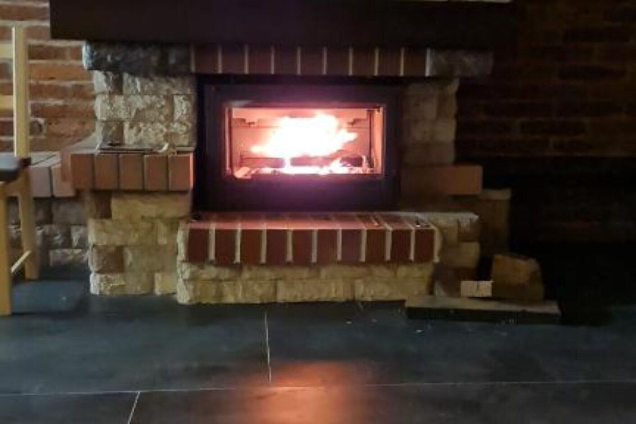 A fireplace with a fire burning inside, surrounded by stone walls and a wooden bench.