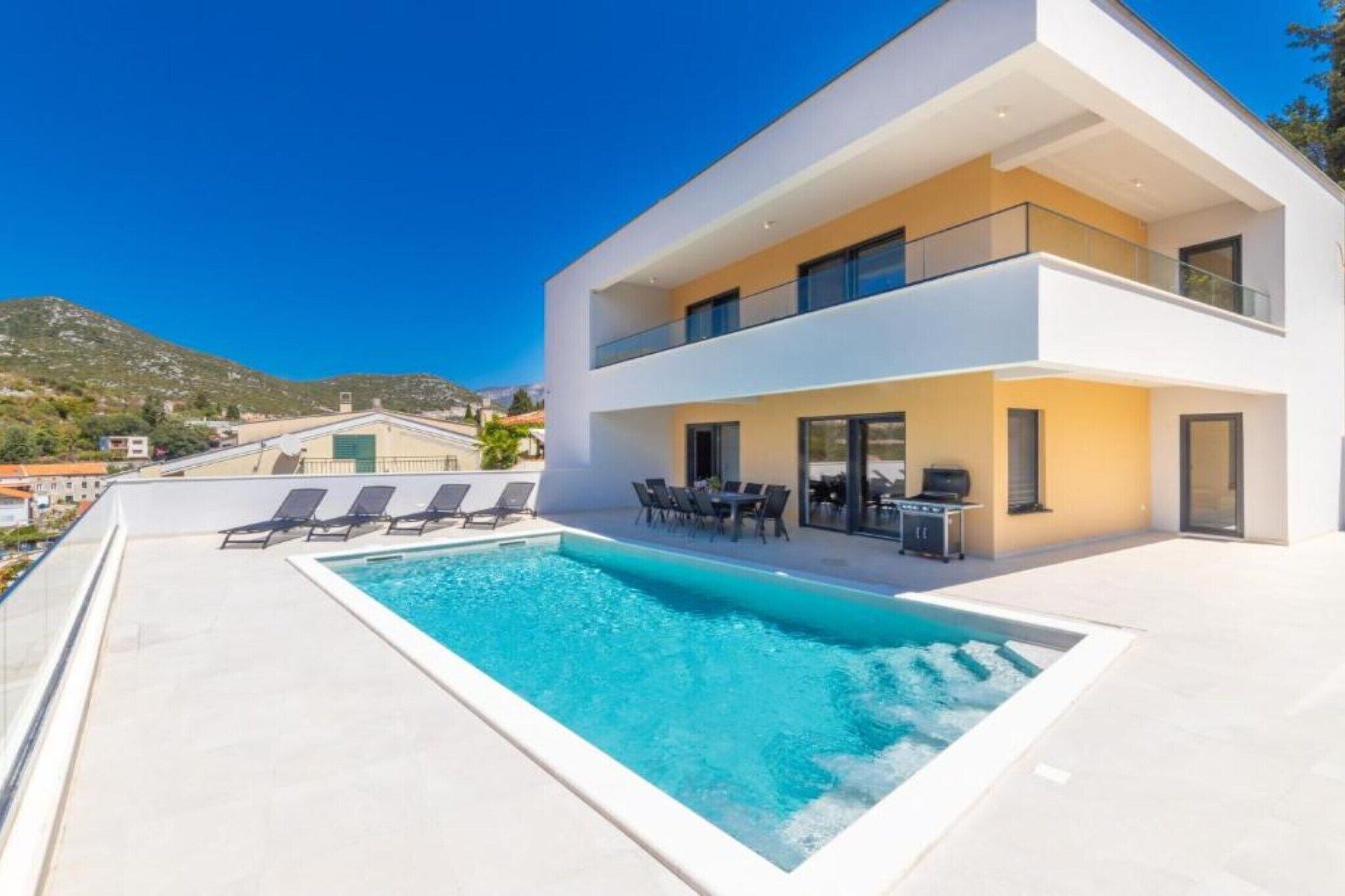 Une maison moderne à deux étages, dotée d’une piscine et d’un espace extérieur aménagé pour se détendre.