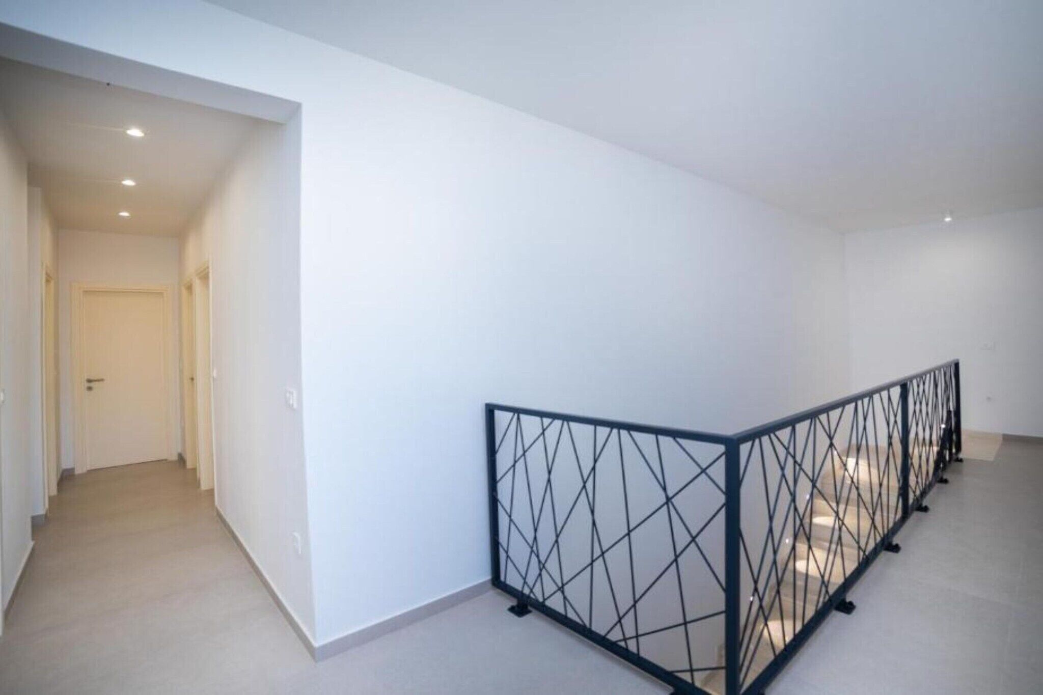 A hallway with a black metal railing, white walls, and a door at the end.
