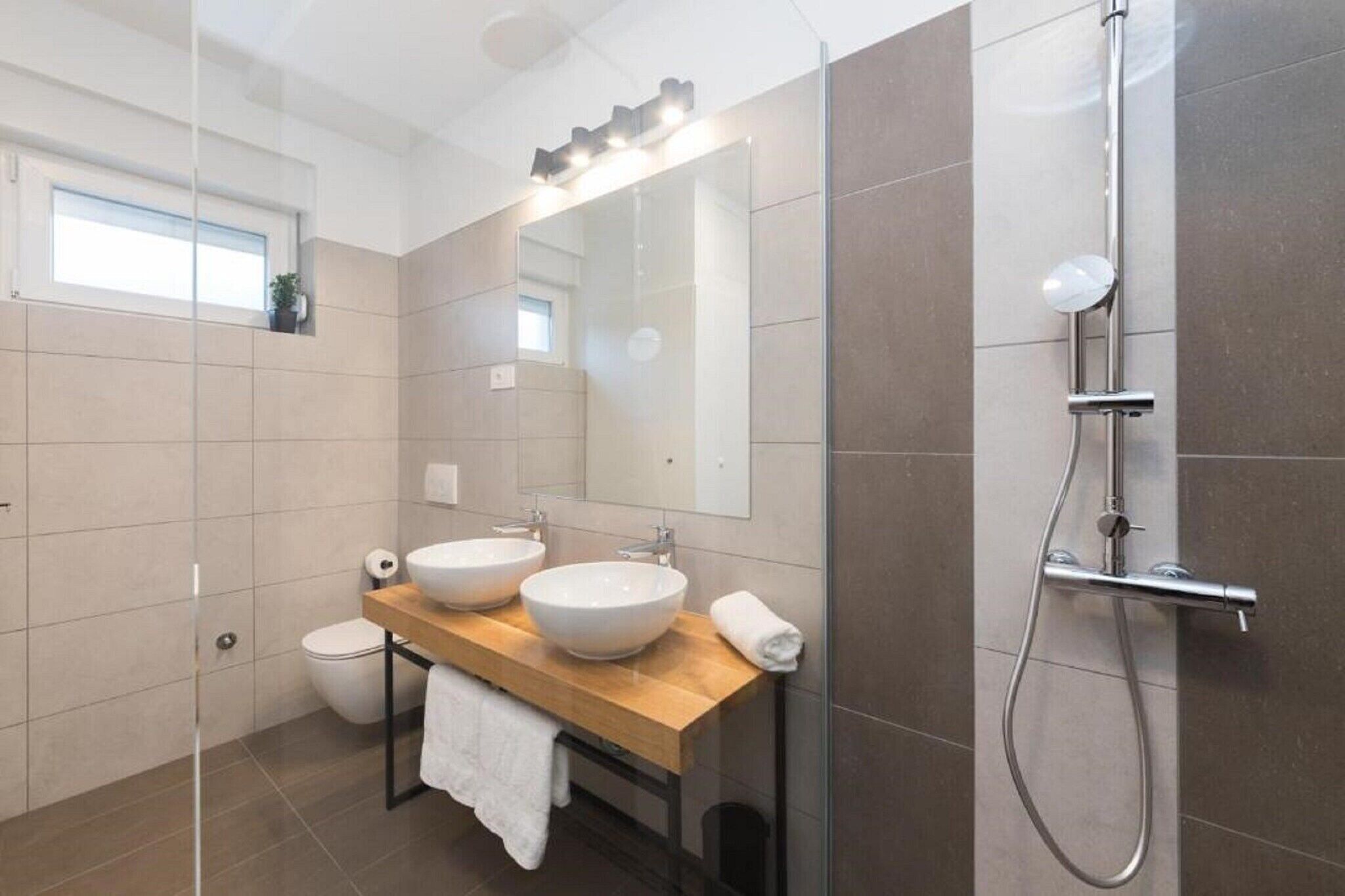 Een moderne badkamer met twee wastafels, een douchecabine van glas en een grote spiegel.