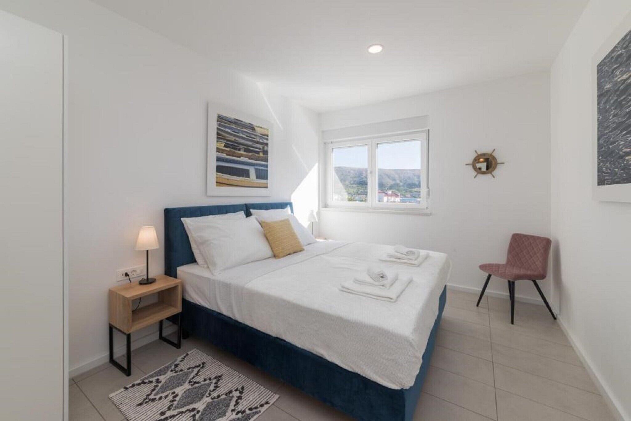 Une chambre à coucher comprenant un lit, une table de chevet, une chaise, une fenêtre et un luminaire fixé au mur.