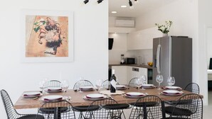A dining area with a wooden table set for six, surrounded by black wire chairs. A modern chandelier hangs above, and a kitchen is visible in the background. - Luxury Villas Bellavista - Four Bedroom Villa with Pool (Pag)