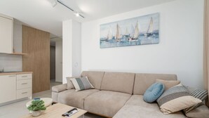 Ein modernes Wohnzimmer mit einem beigen Sofa, einem Couchtisch mit einer Pflanze und einem Gemälde von Segelbooten an der Wand.