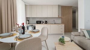 Eine moderne Küche mit hellen Schränken, ein Essbereich mit Tisch für zwei Personen und ein Sofa im Wohnbereich.