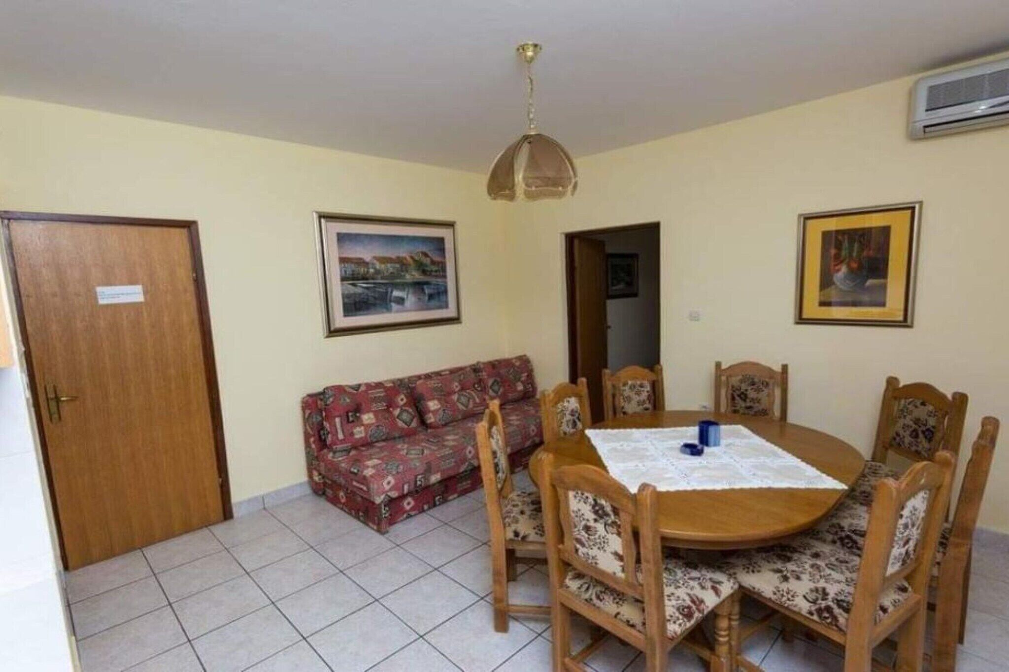 Un comedor con una mesa redonda de madera, sillas con estampado floral, un sofá y una lámpara en el techo.