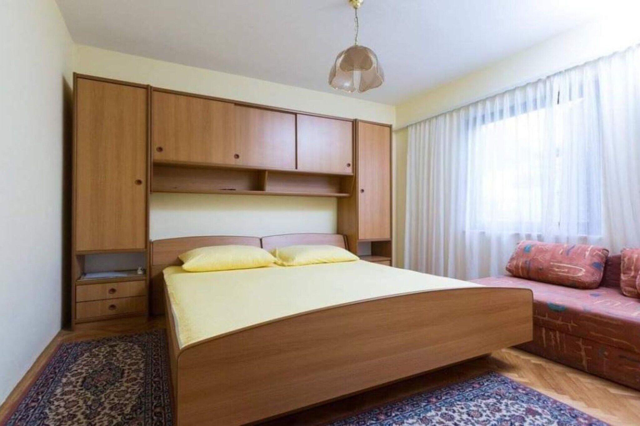 A bedroom with a wooden bed, a nightstand, a built-in wardrobe, and a sofa with cushions.