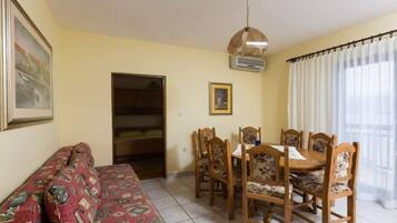 A room with a sofa, dining table, chairs, an air conditioning unit, and a door.