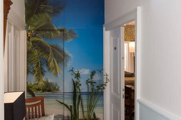 A room with a mural of a beach scene, a wooden chair, and a potted plant.