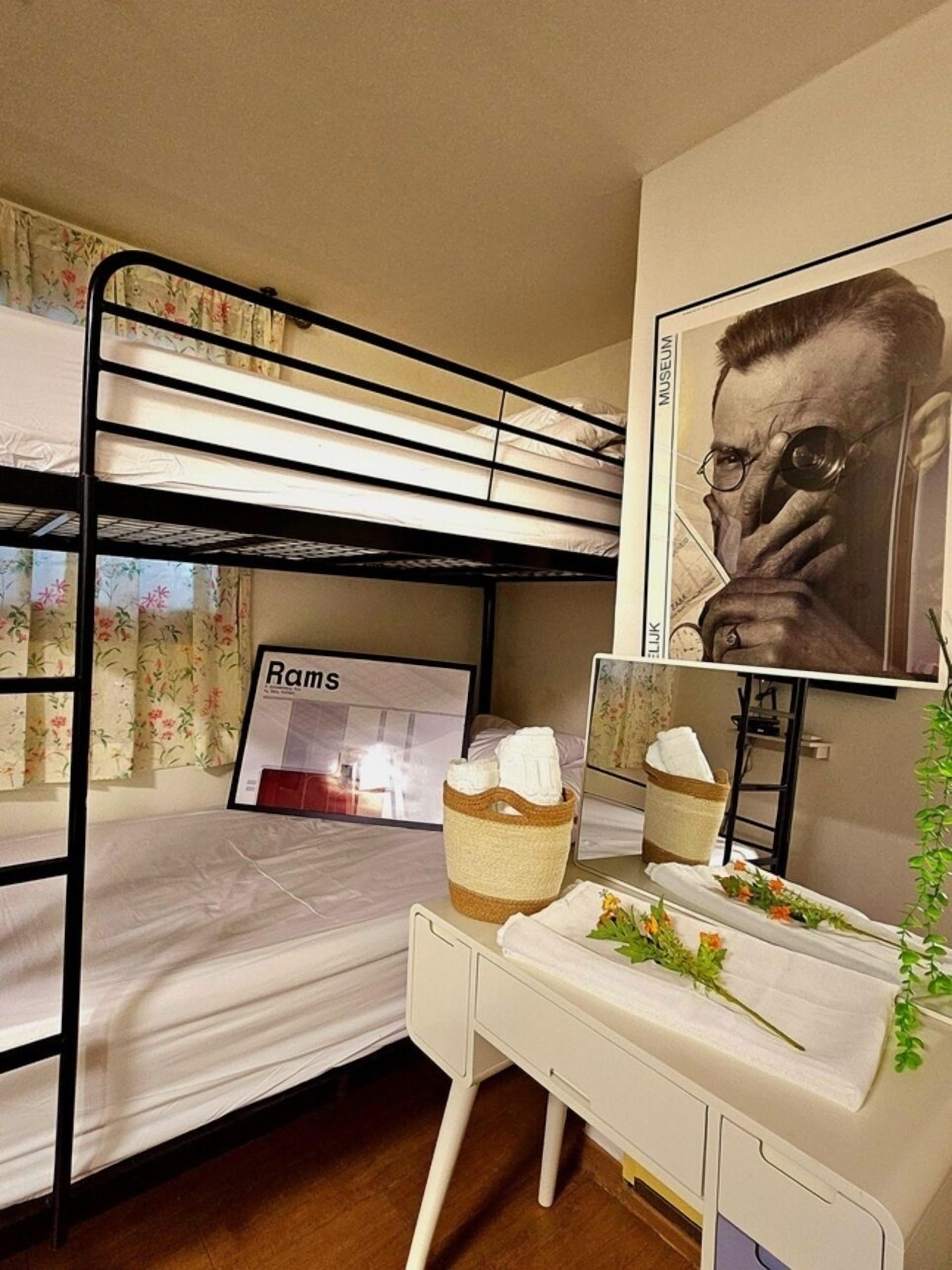 A bunk bed with a framed picture of a person, a small desk with a basket, and a wall-mounted mirror.