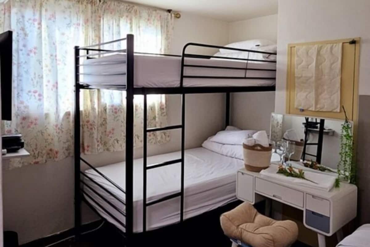 A bunk bed room with a desk, chair, and a small stool.