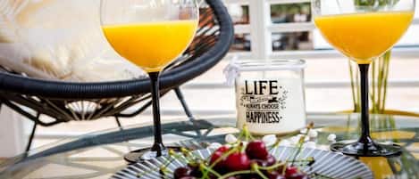 Two glasses of orange juice on a glass table with a glass candle and cherries.