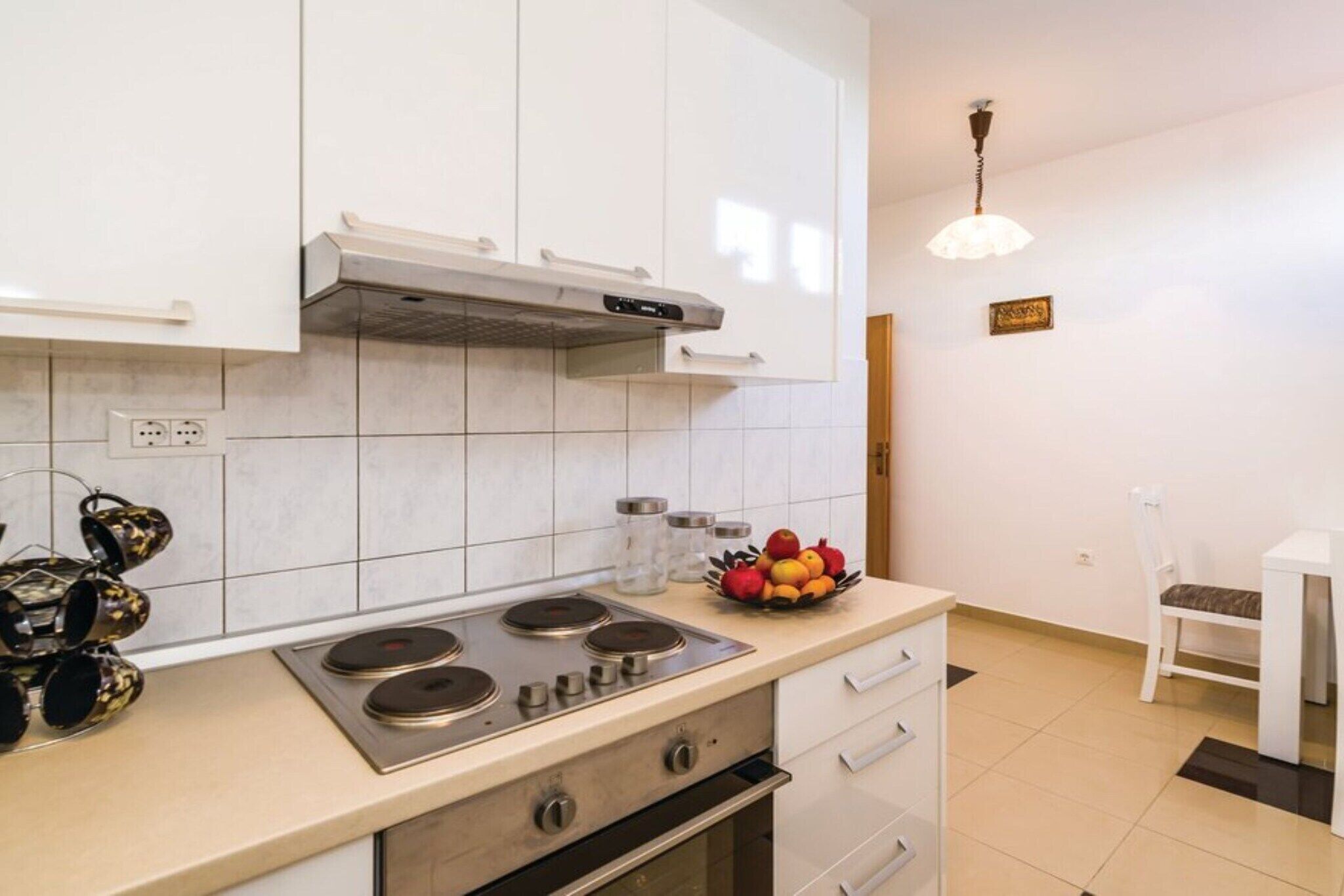 Una cucina moderna con mobili bianchi, un piano cottura a gas e una ciotola di frutta sul bancone.
