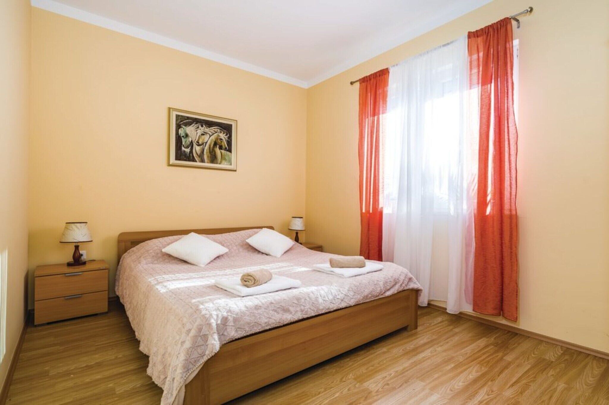 Una camera da letto con un letto in legno, due comodini con lampade, un quadro appeso al muro e tende rosse.
