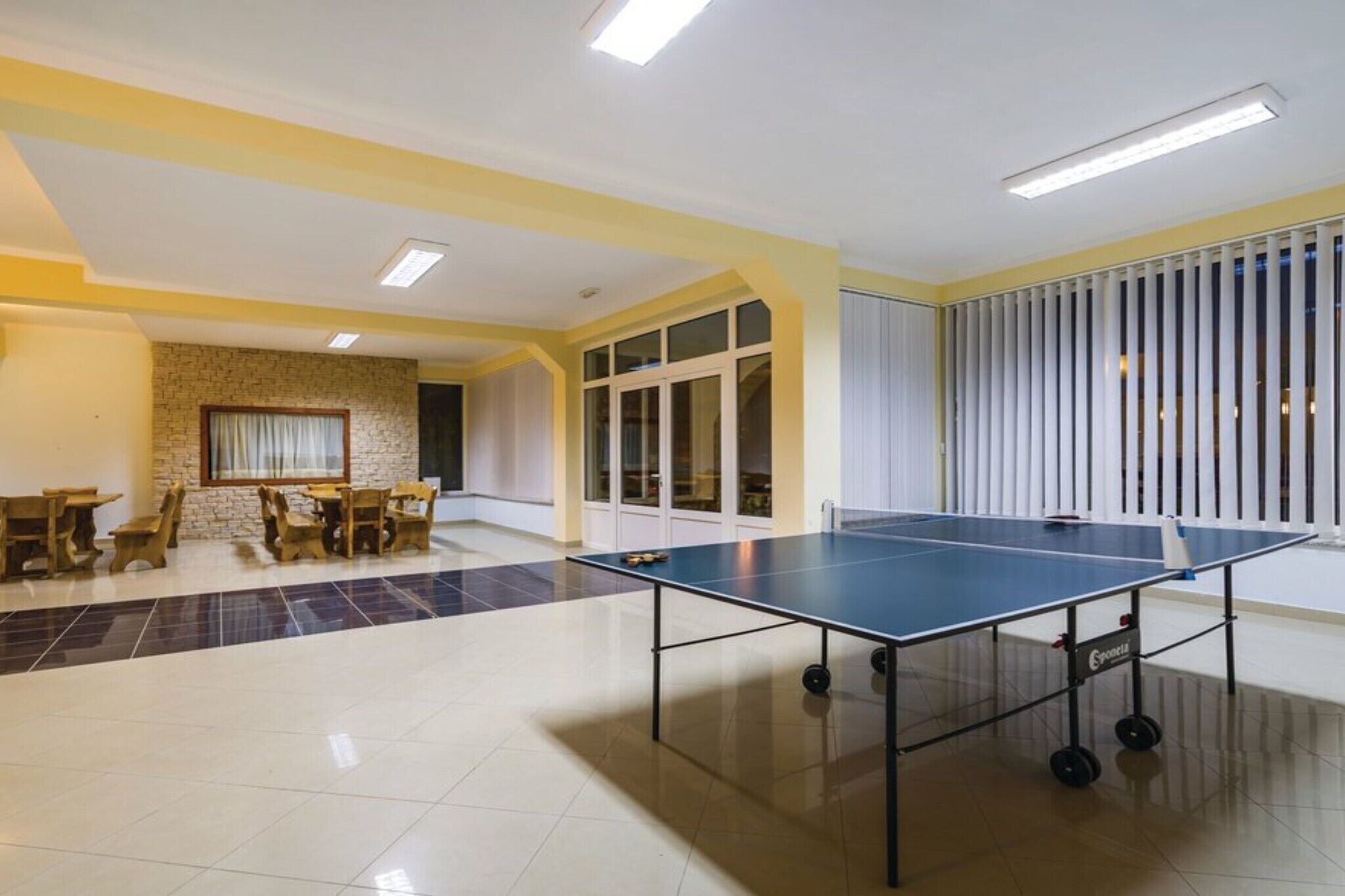 A spacious room with a ping pong table, a dining area with chairs, and a large window with blinds.