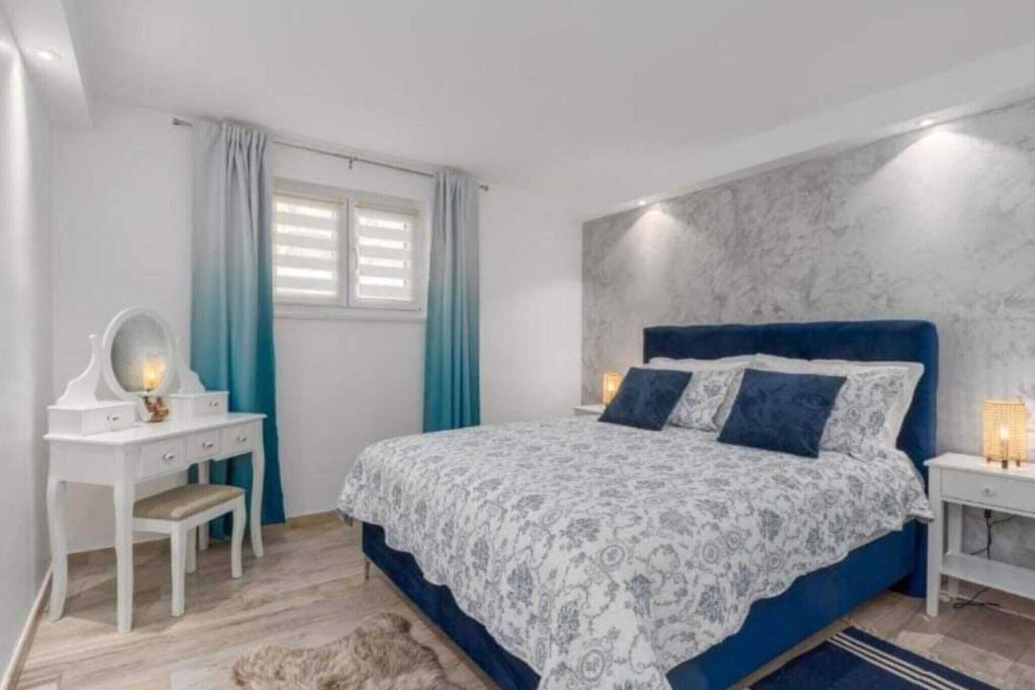 A bedroom with a bed, a vanity with a mirror, and a window with curtains.