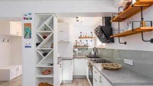Cocina moderna con armarios blancos, horno empotrado y encimera gris. Hay estantes de madera sobre el fregadero y una cesta en la encimera.