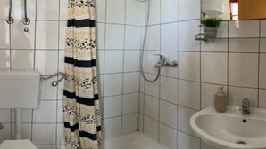 A bathroom with a toilet, sink, shower, and a patterned shower curtain. - Apartments Fortuna - Studio Apartment with Balcony (Biograd na Moru)