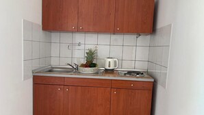 A compact kitchen with wooden cabinets, a white tiled backsplash, a sink, a kettle, and a fruit bowl. - Apartments Fortuna - Studio Apartment with Balcony (Biograd na Moru)