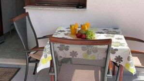 A dining table with a floral tablecloth, a chair, and a fruit basket containing oranges, grapes, and apples. - One Bedroom Apartment with Balcony (3) (Biograd na Moru)