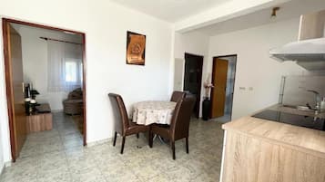 Ein Essbereich mit rundem Tisch und Stühlen, eine Küche mit Herd und Spüle sowie ein Flur, der zum Schlafzimmer führt.