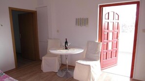 A small, bright room with a round table and two chairs, a bottle of wine, and a red door. - One Bedroom apartment with Terrace (Šibenik)