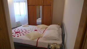 A neatly made bed with a white and red floral bedspread, a bedside table with a teapot, and a wooden wardrobe in the background. - One Bedroom apartment with Terrace (Šibenik)