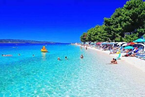 A beach with clear blue water, people swimming and sunbathing, and umbrellas on the sand.