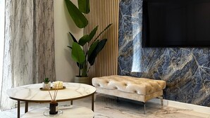 Een moderne woonkamer met een marmeren vloer, een gestofte bank, een ronde tafel met een vaas en een grote plant.